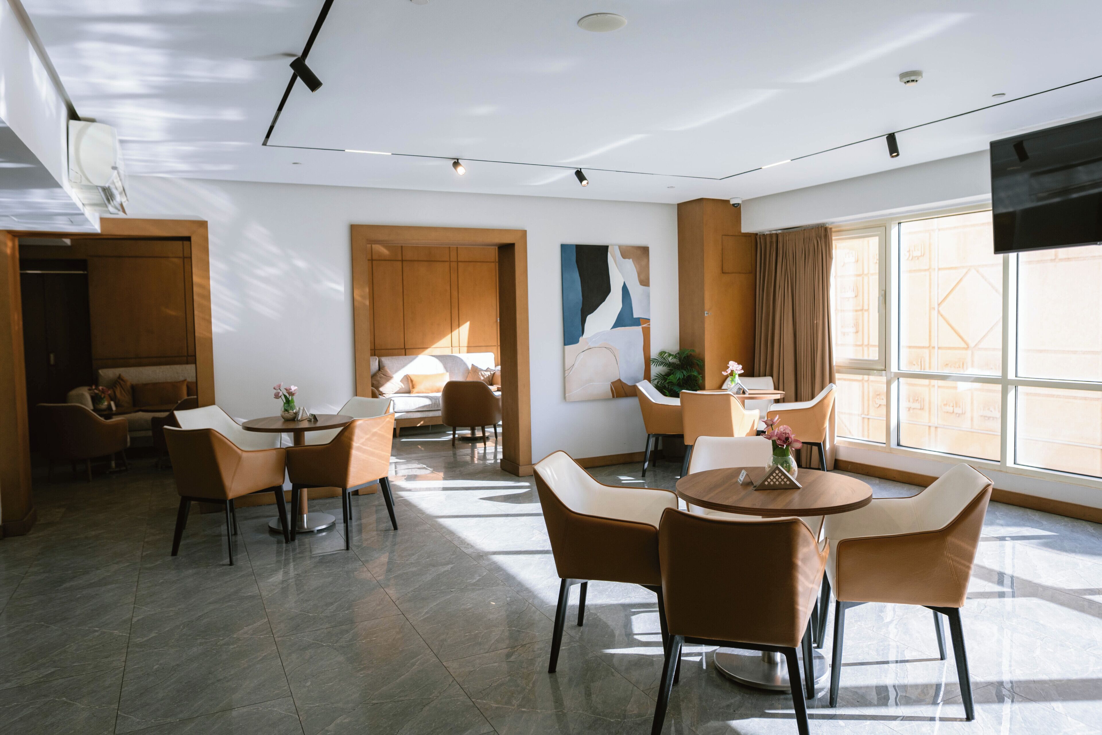 Een moderne hotellobby met een zithoek, een groot raam en een aan de muur bevestigde flatscreen televisie.