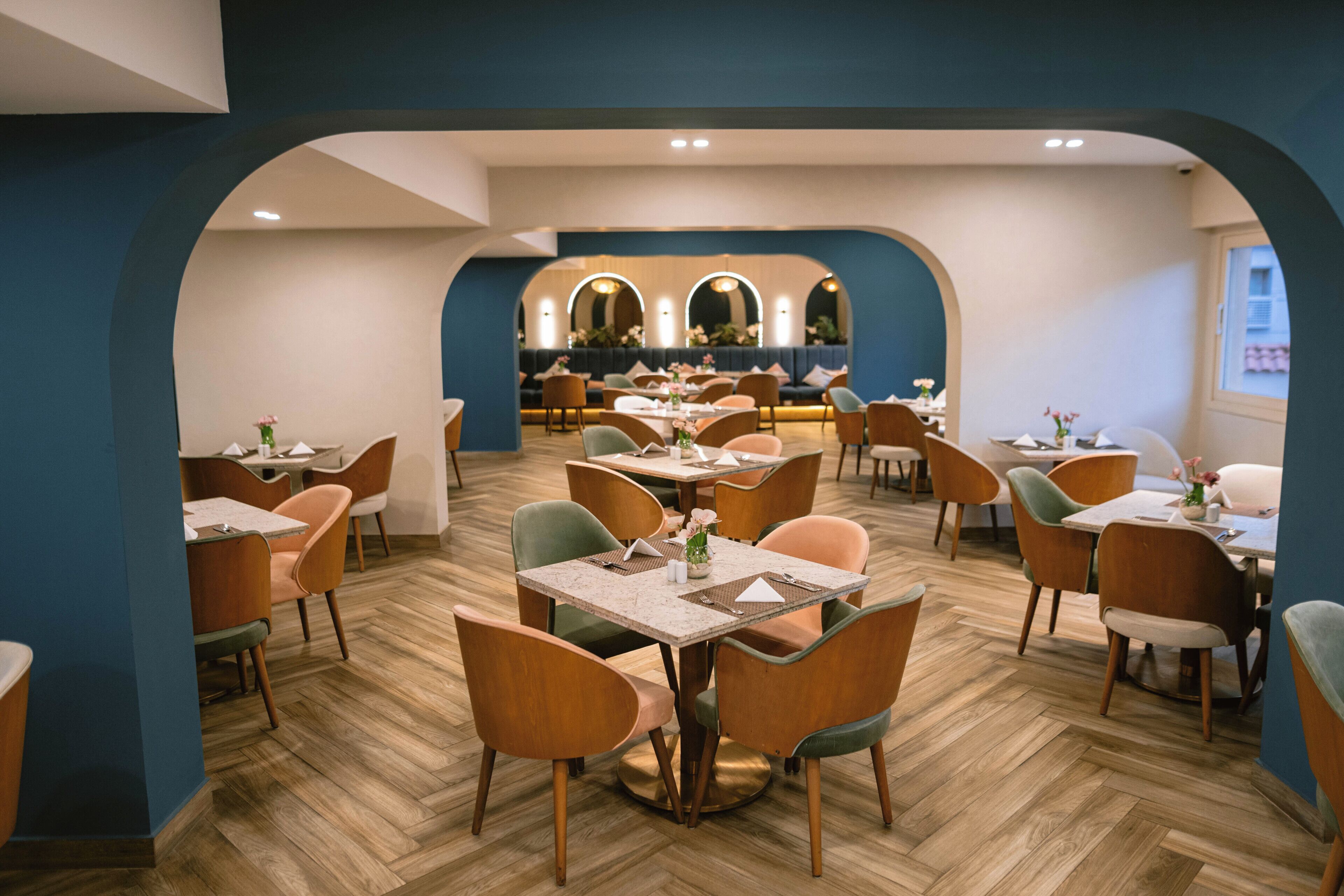 A restaurant with multiple tables and chairs, a herringbone floor pattern, and a blue accent wall.