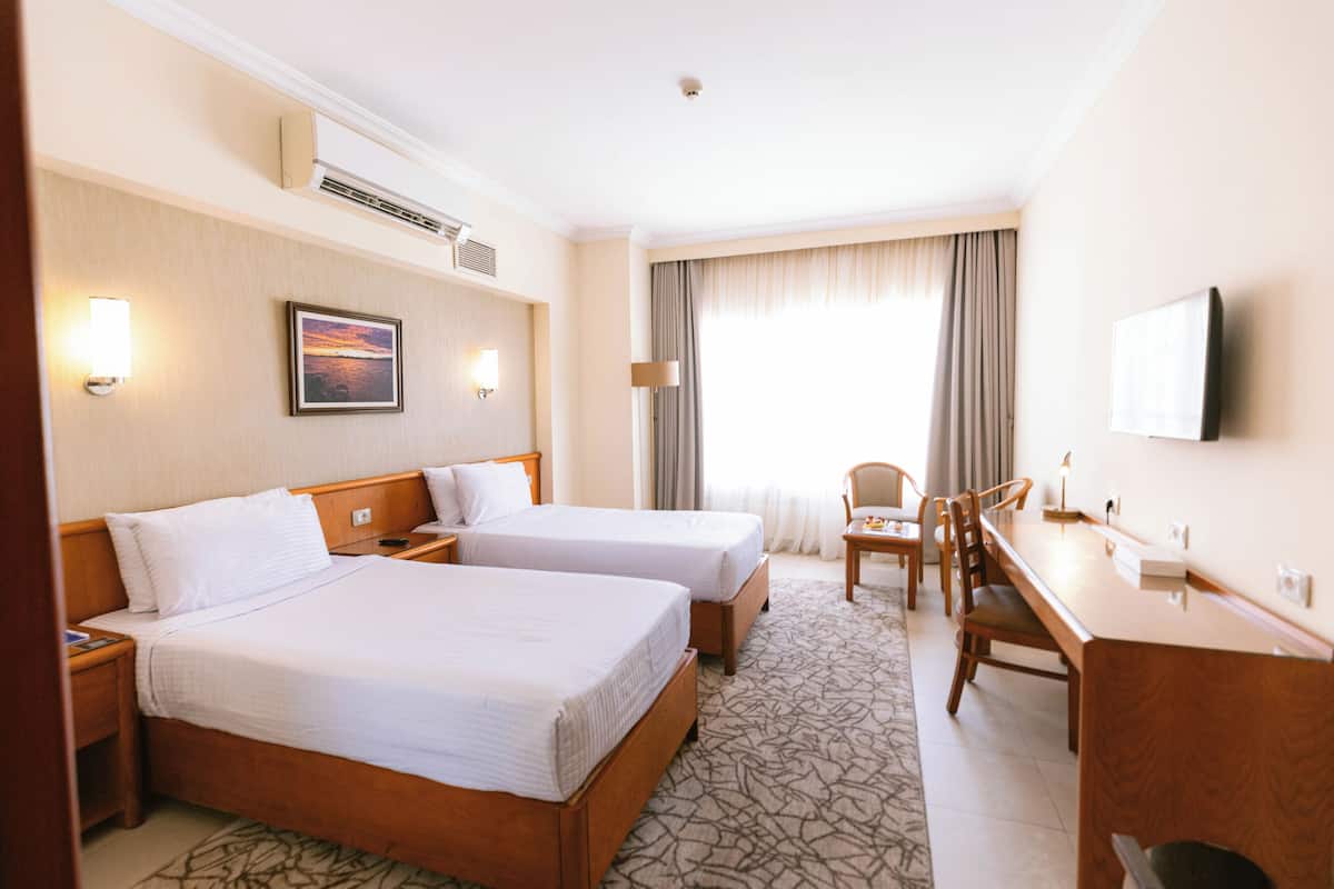 A hotel room with two beds, a desk, a chair, a TV, and a window with curtains.