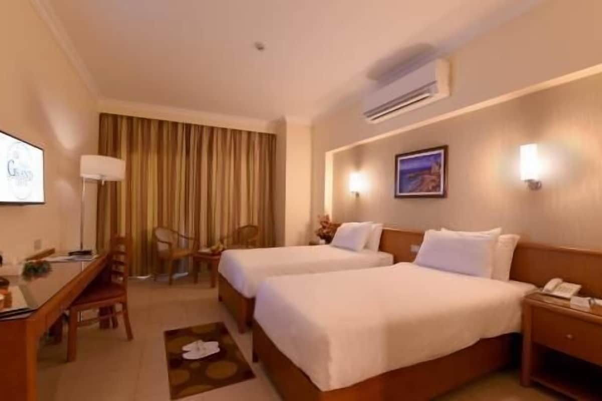 Habitación de hotel con dos camas, un escritorio, una silla, una lámpara de escritorio y un aire acondicionado de pared.