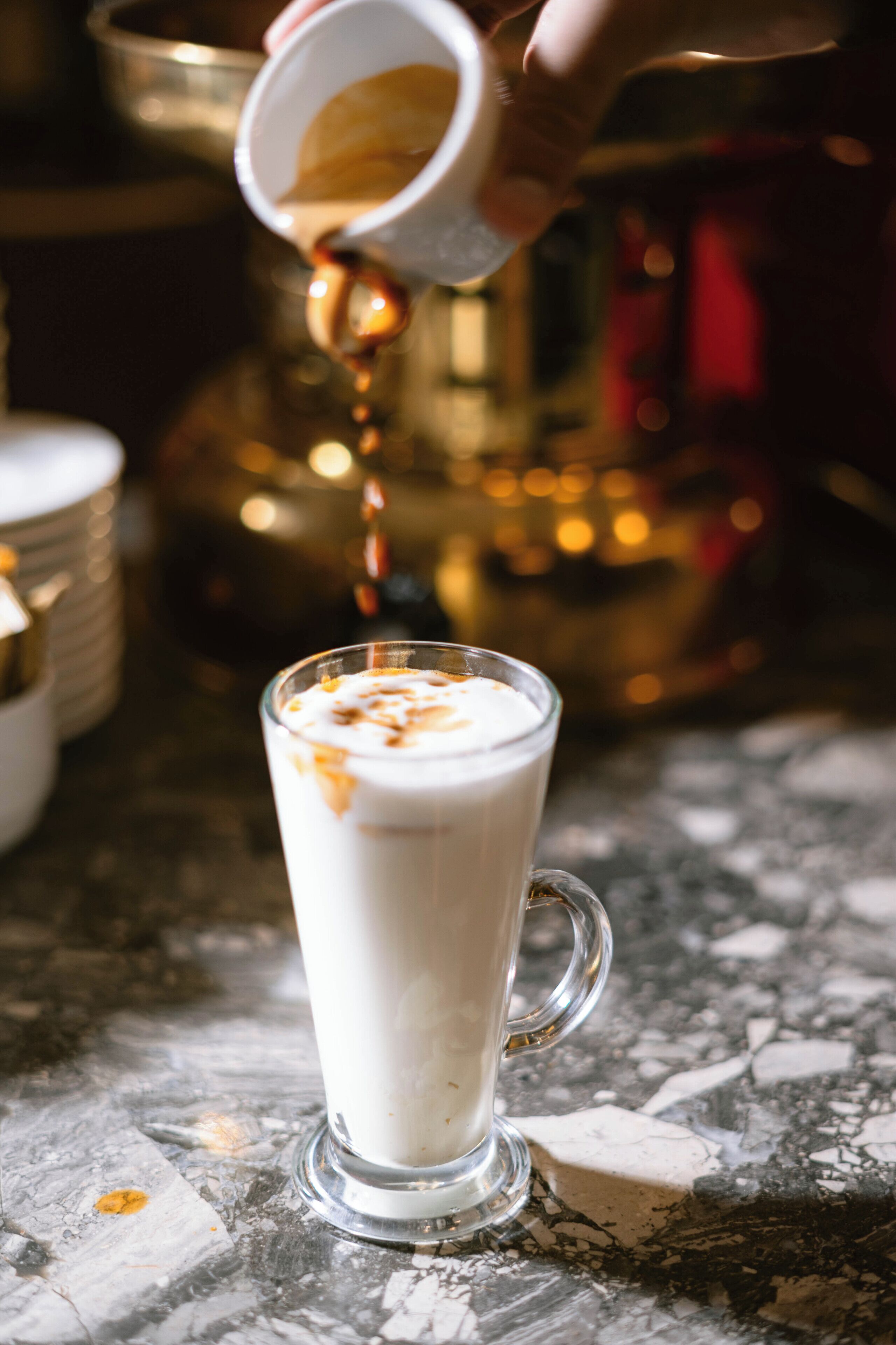 A clear glass mug on a marble surface with a hand pouring a liquid into it.