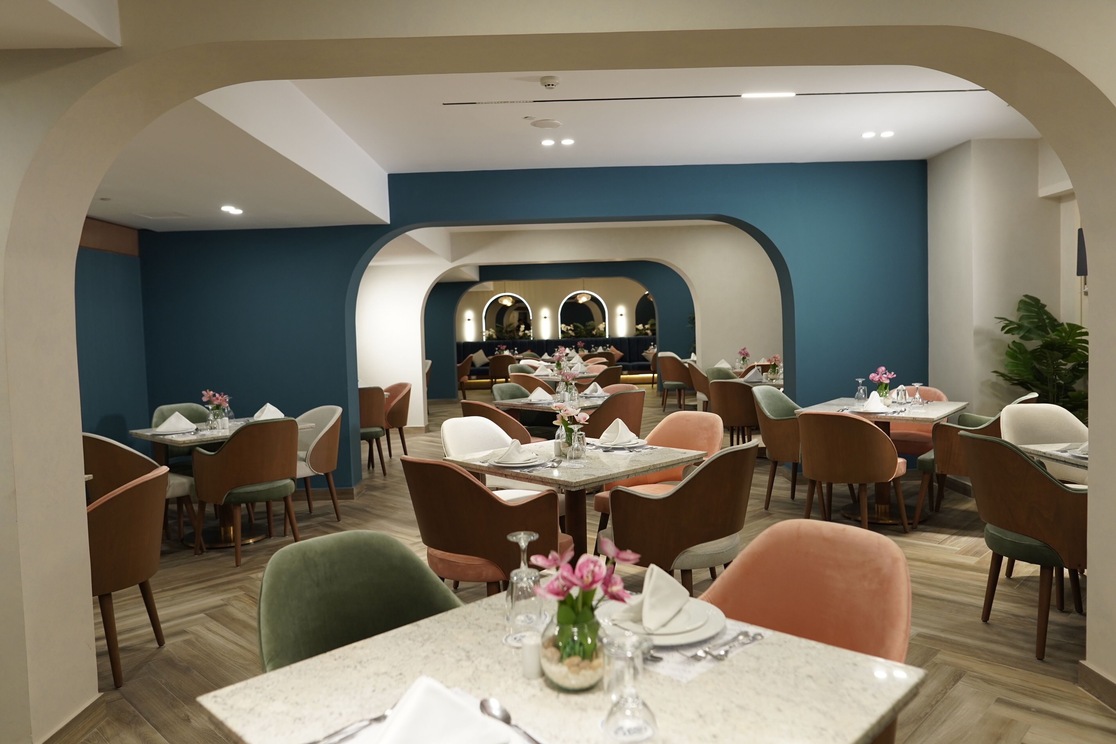 Un vaste espace dédié à la salle à manger, doté de nombreuses tables et chaises, et présentant un aménagement intérieur moderne avec des murs bleus et un plancher en bois.
