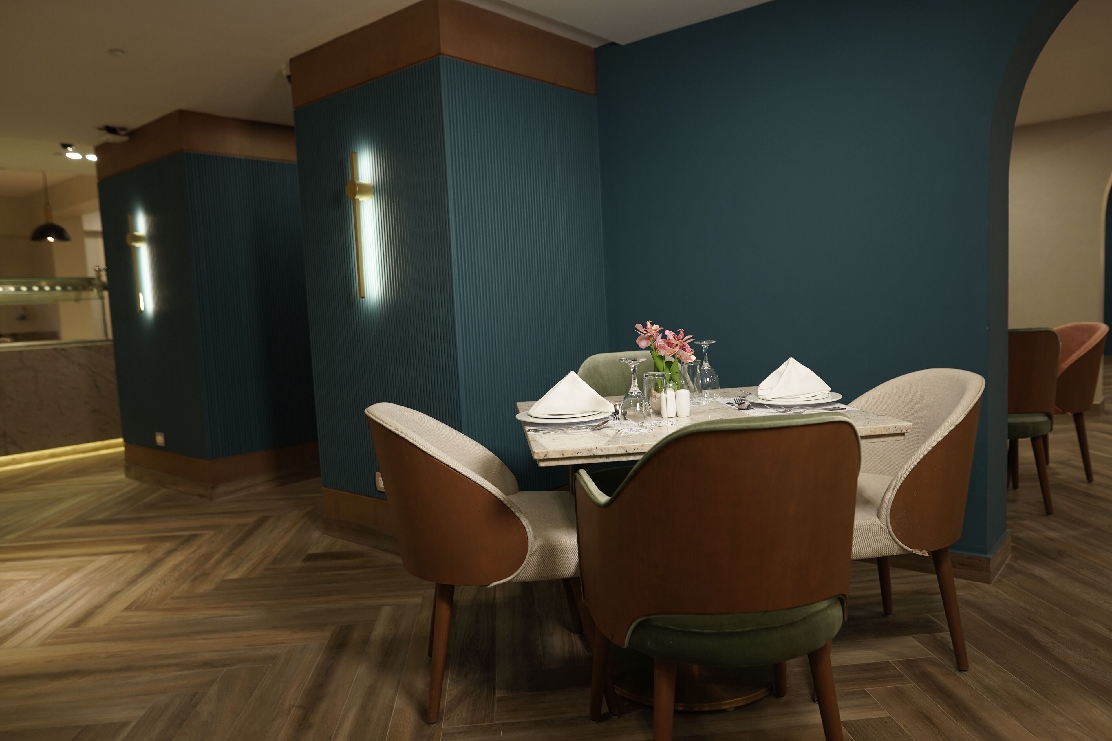 Comedor con una mesa dispuesta para cuatro personas, rodeada de sillas modernas, en una habitación con paredes color turquesa y suelo de madera.