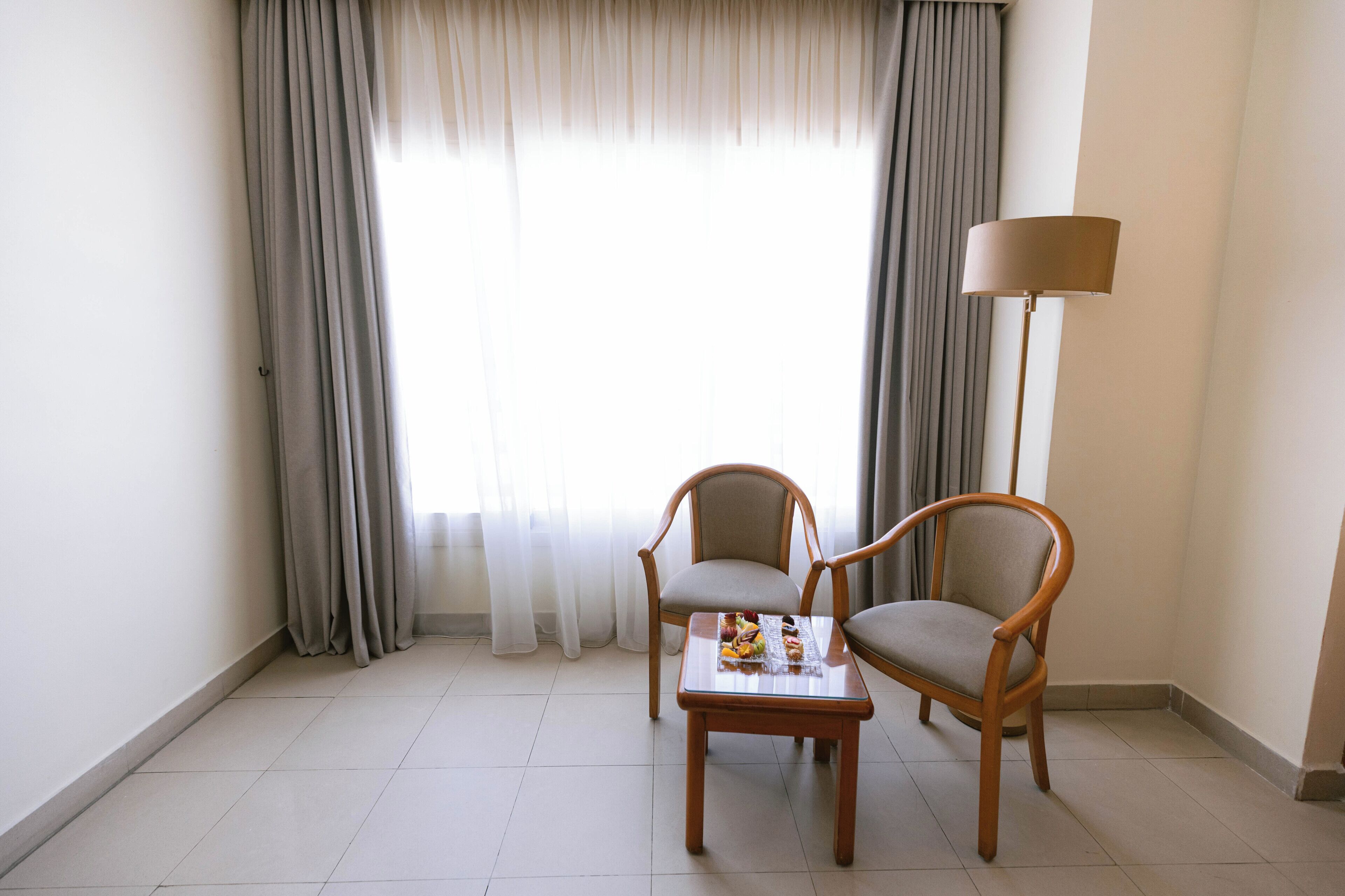 A room with two wooden chairs, a small table with a tray, and a floor lamp.