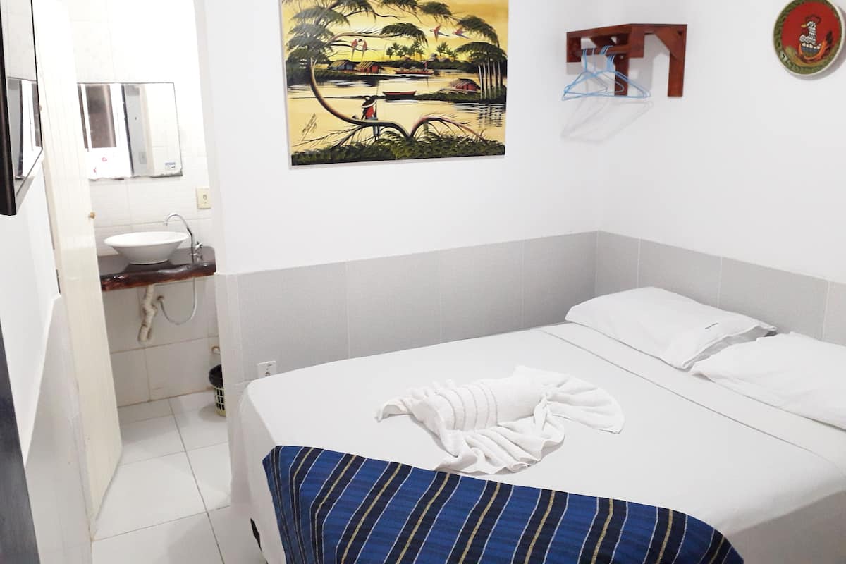 A bedroom with a bed, a painting, a sink, and a mirror.