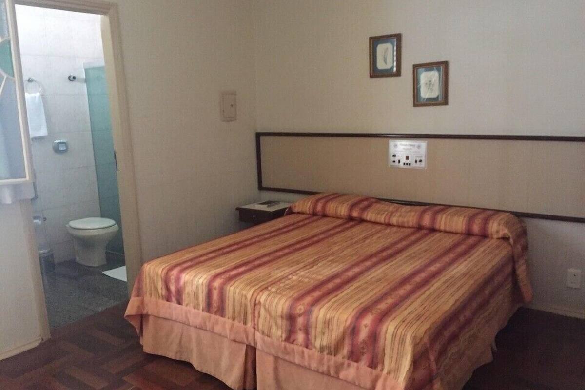 A hotel room with a bed, a nightstand, and a wall-mounted power outlet.