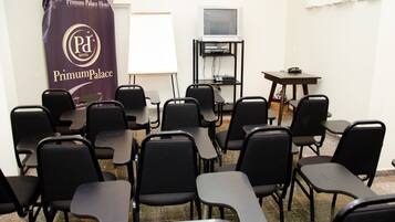 A conference room with rows of black chairs, a whiteboard, a television on a stand, and a banner for the Premium Palace Hotel.