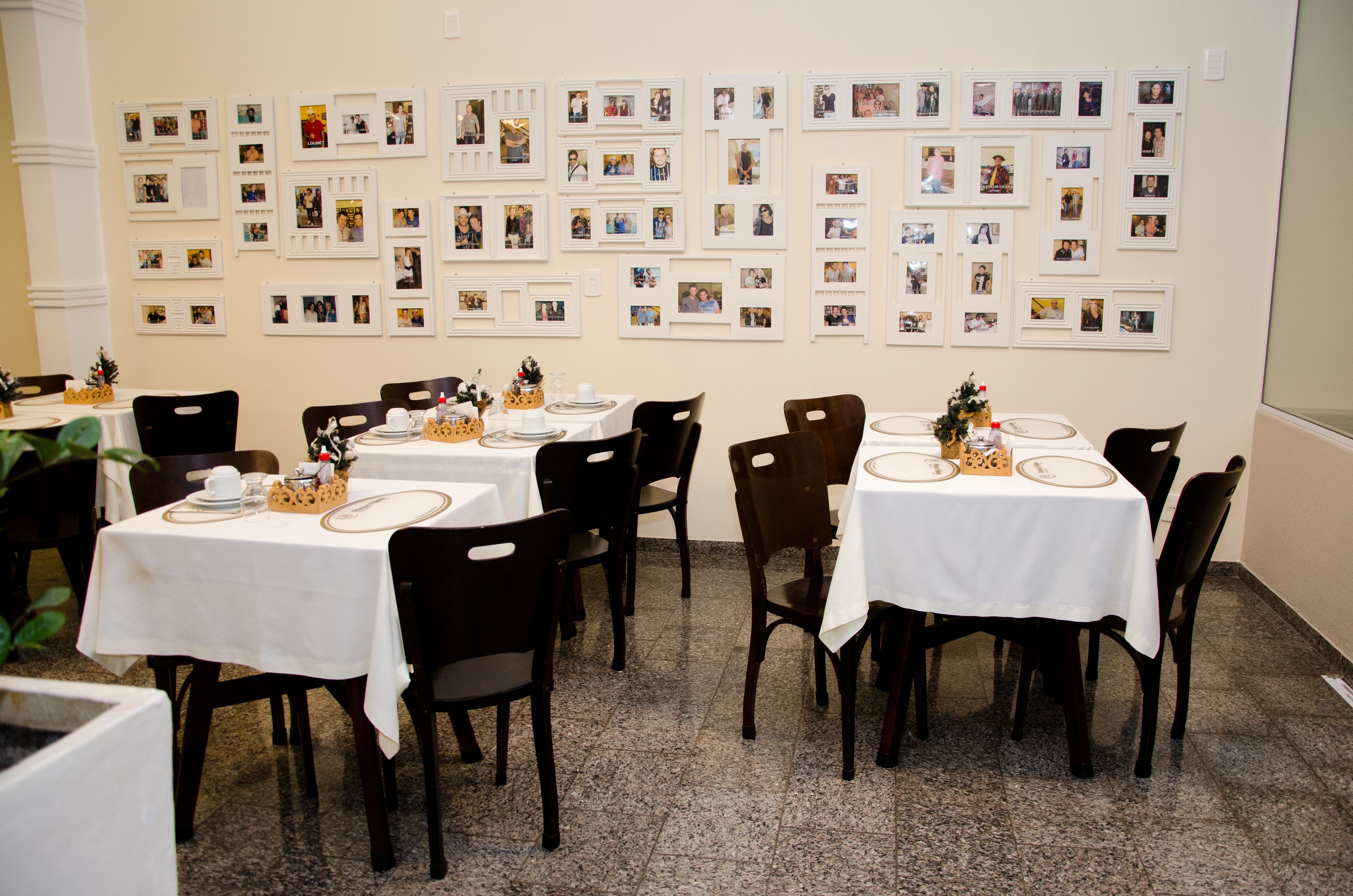 Comedor con mesas dispuestas para cuatro, cada una con mantel blanco y sillas oscuras. Las paredes están decoradas con numerosas fotografías enmarcadas.
