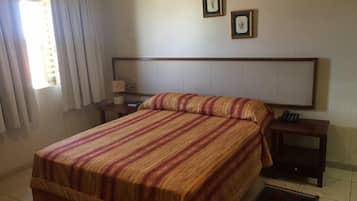 A hotel room with a bed, a nightstand, a lamp, and two framed pictures on the wall.