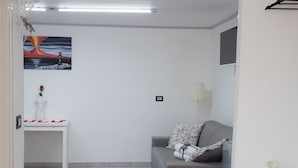 Un salon moderne avec un canapé gris, une petite table d’appoint blanche, une plante en pot et un tableau accroché au mur.