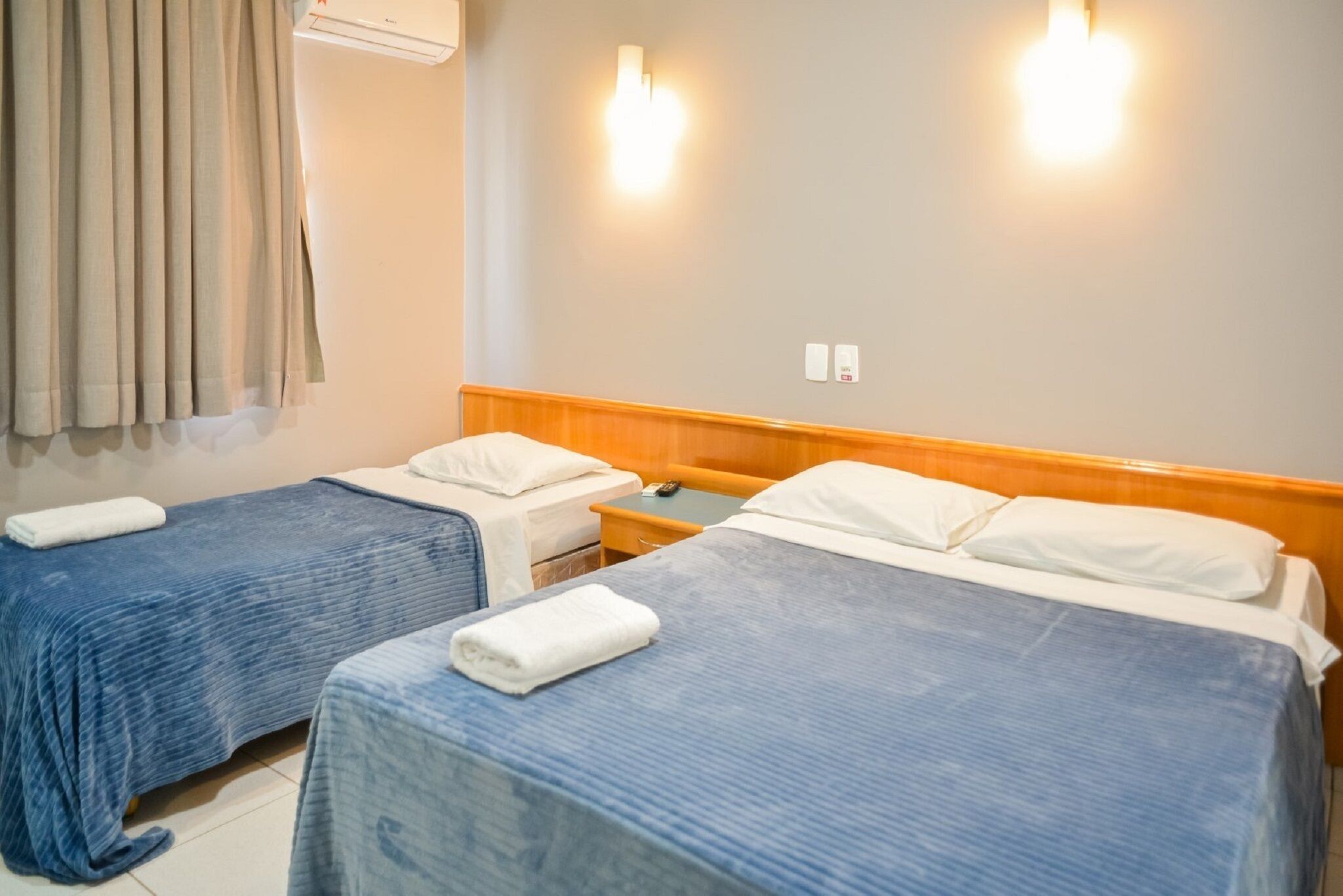A hotel room with two beds, a wooden headboard, a nightstand, a telephone, and a wall-mounted light fixture.