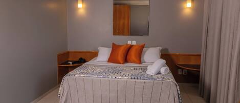 A hotel room with a bed, two nightstands, a mirror, and a curtain.