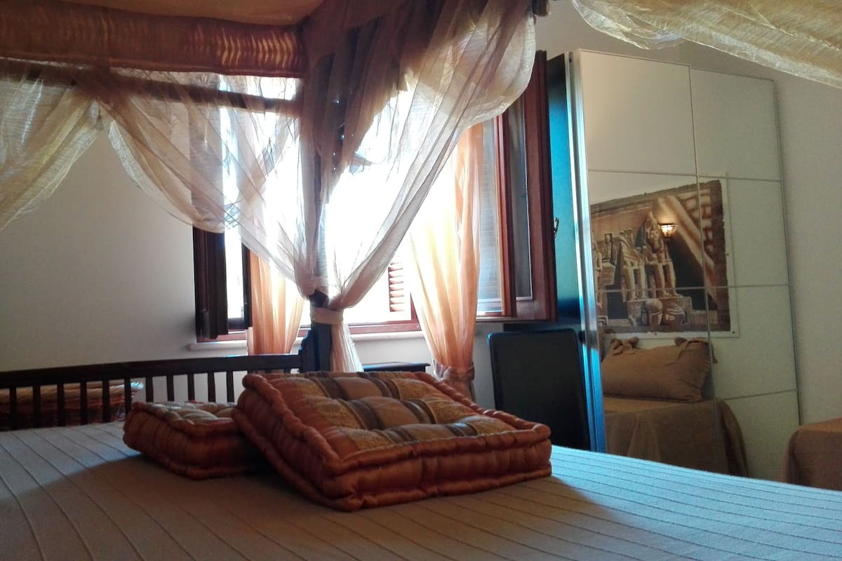 A bedroom with a wooden bed, a canopy, and a window with curtains.