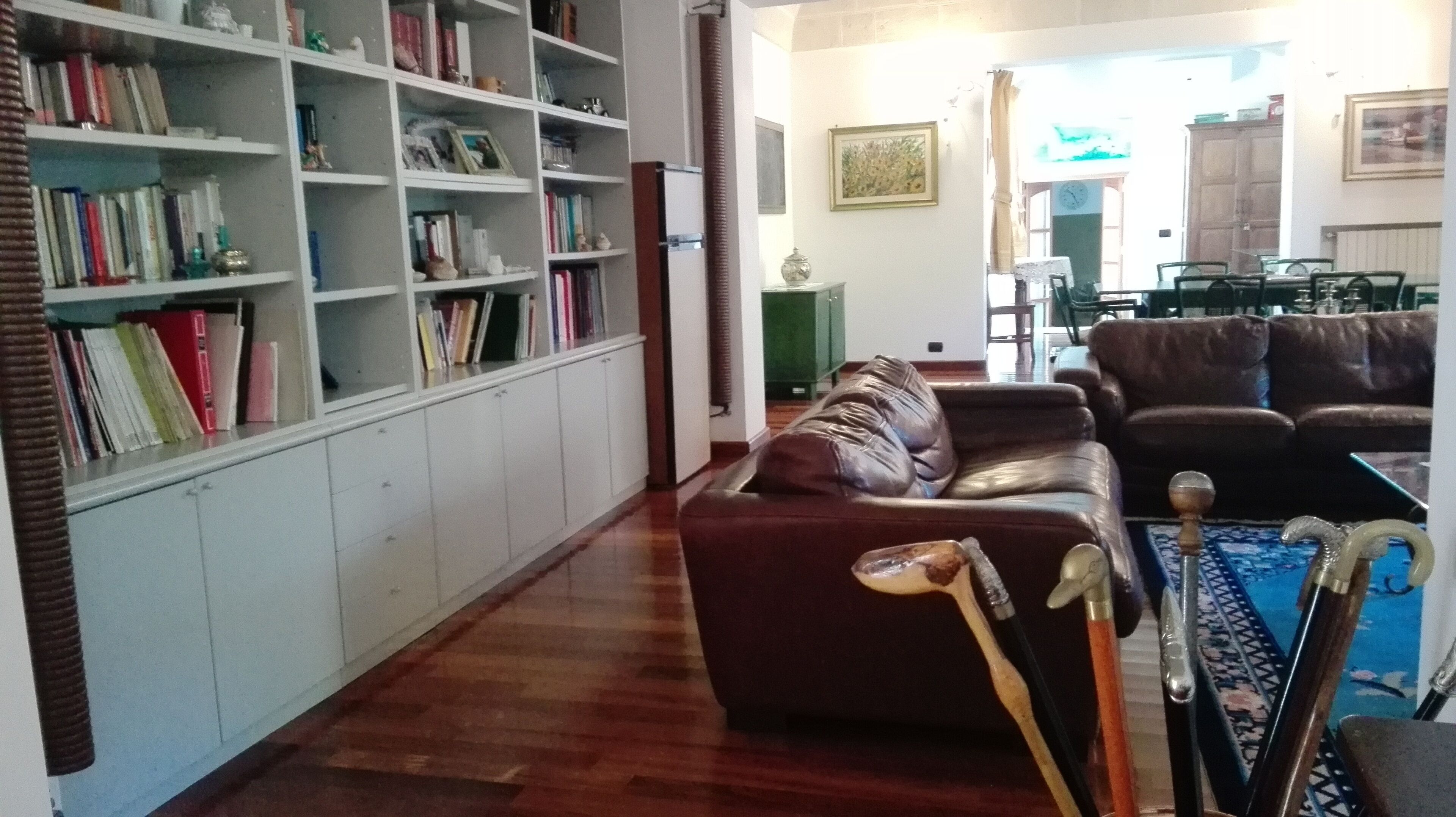 A living room with a brown sofa, a bookshelf filled with books, and a dining area with a table and chairs.