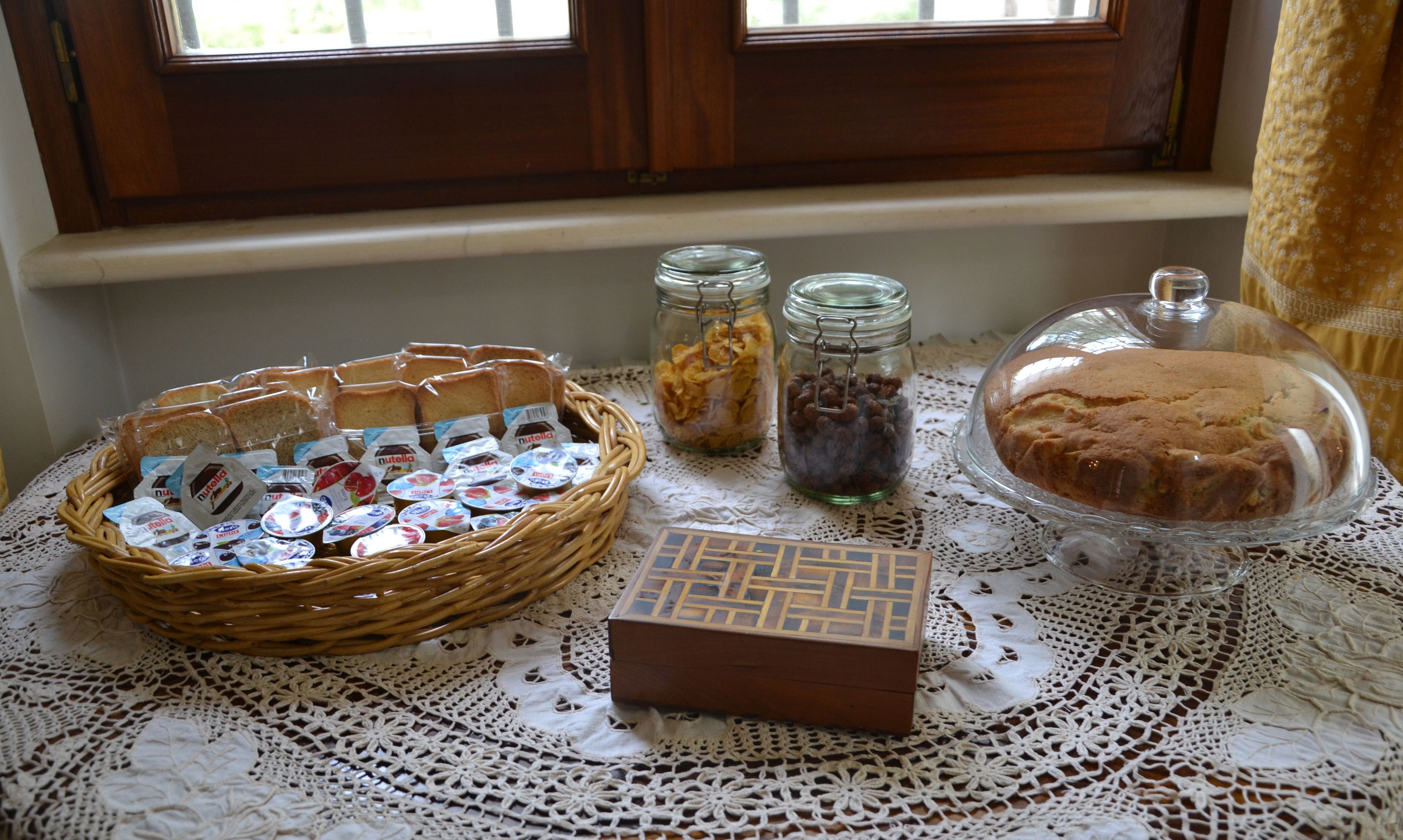 Een tafel met een rieten mand vol brood, potjes met snacks, een chocoladereep en een taart.