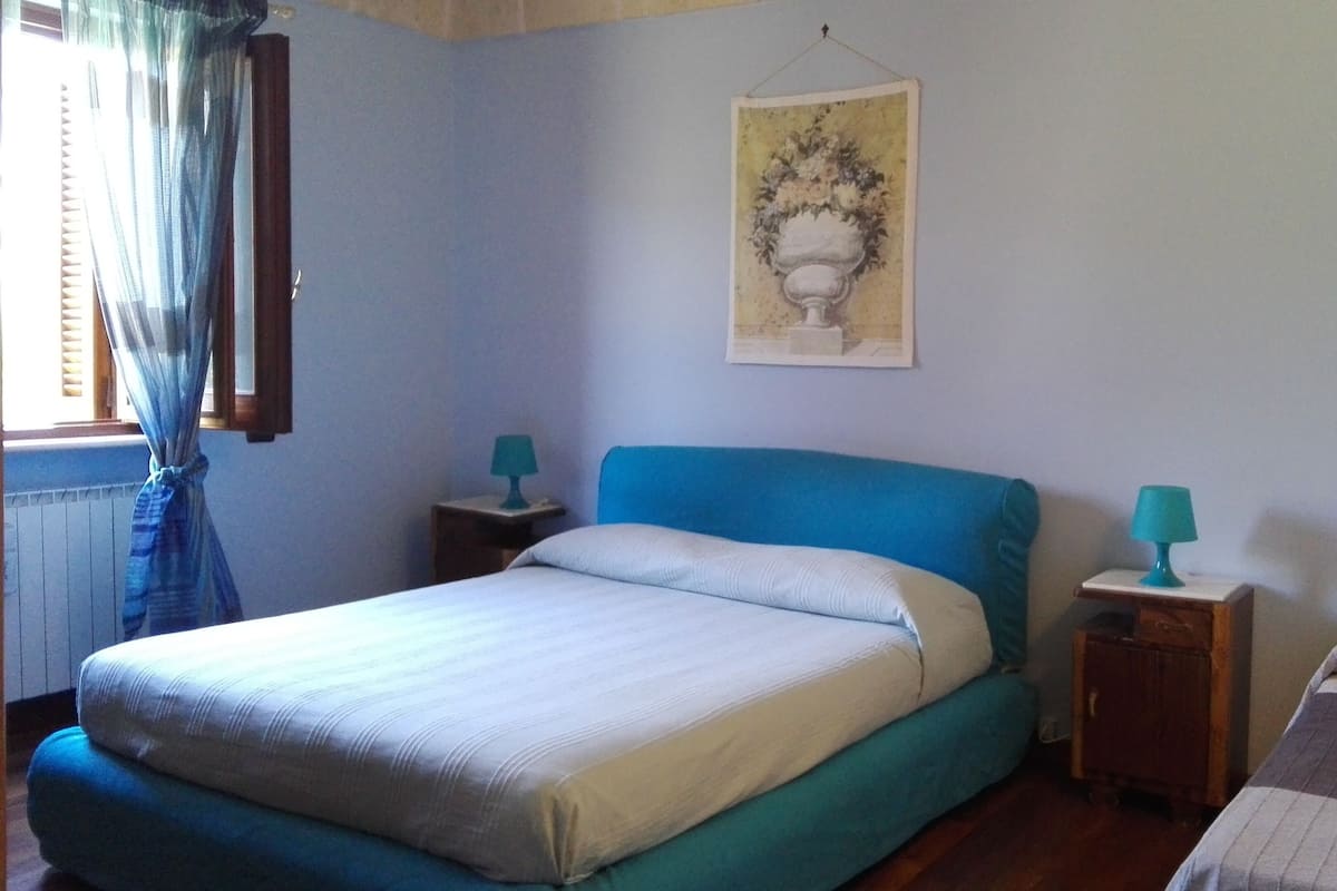 A bedroom with a single bed, a nightstand, a small table, and a window with curtains.