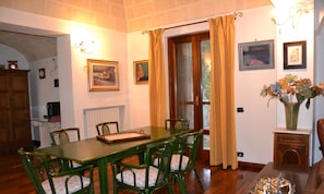 A dining area with a wooden table and chairs, a vase with flowers, and framed artwork on the walls.