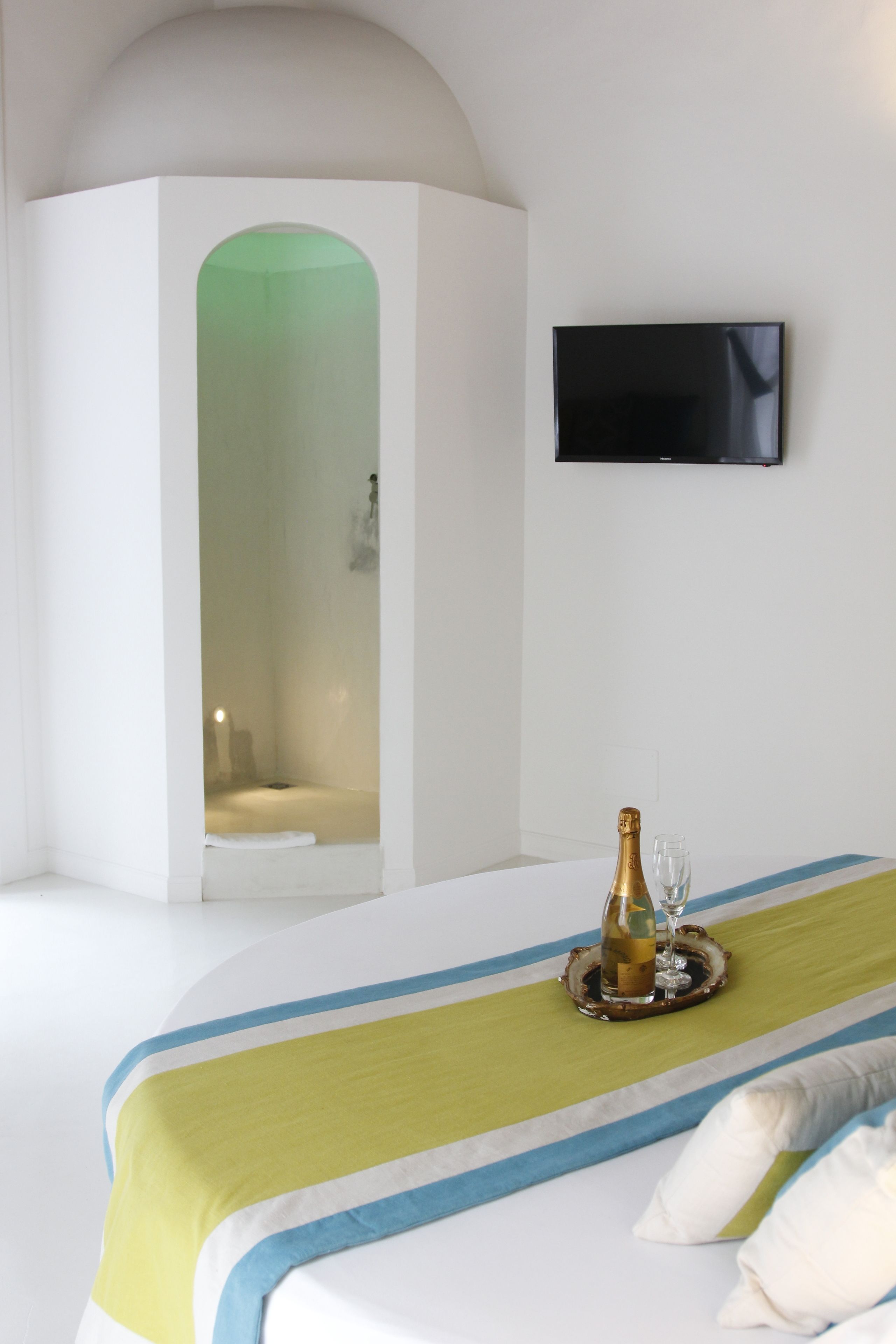 Une chambre d’hôtel moderne avec un grand lit, un téléviseur fixé au mur et une bouteille de champagne posée sur le lit.