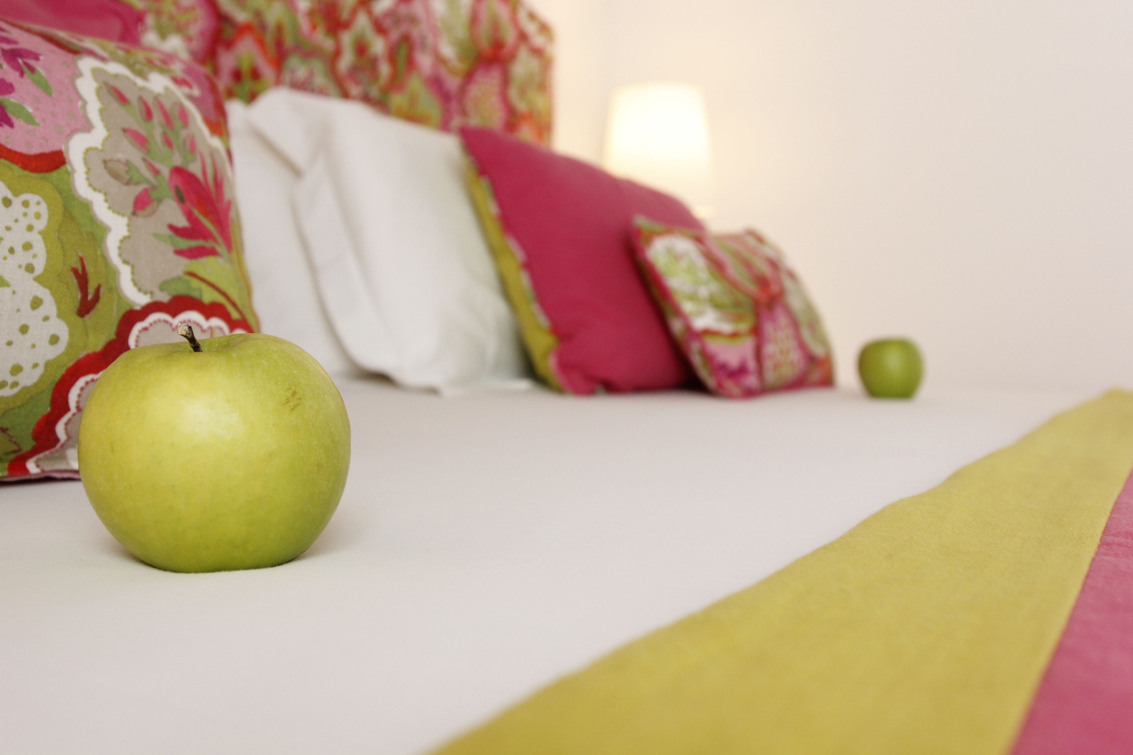 A bed with a green apple on it, a white pillow, and a green apple on the floor.