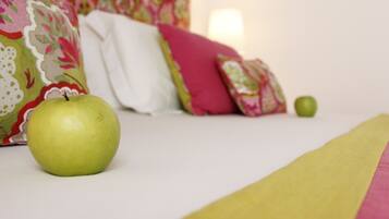Una cama con una manzana verde encima, un almohadón blanco y otra manzana verde en el suelo.
