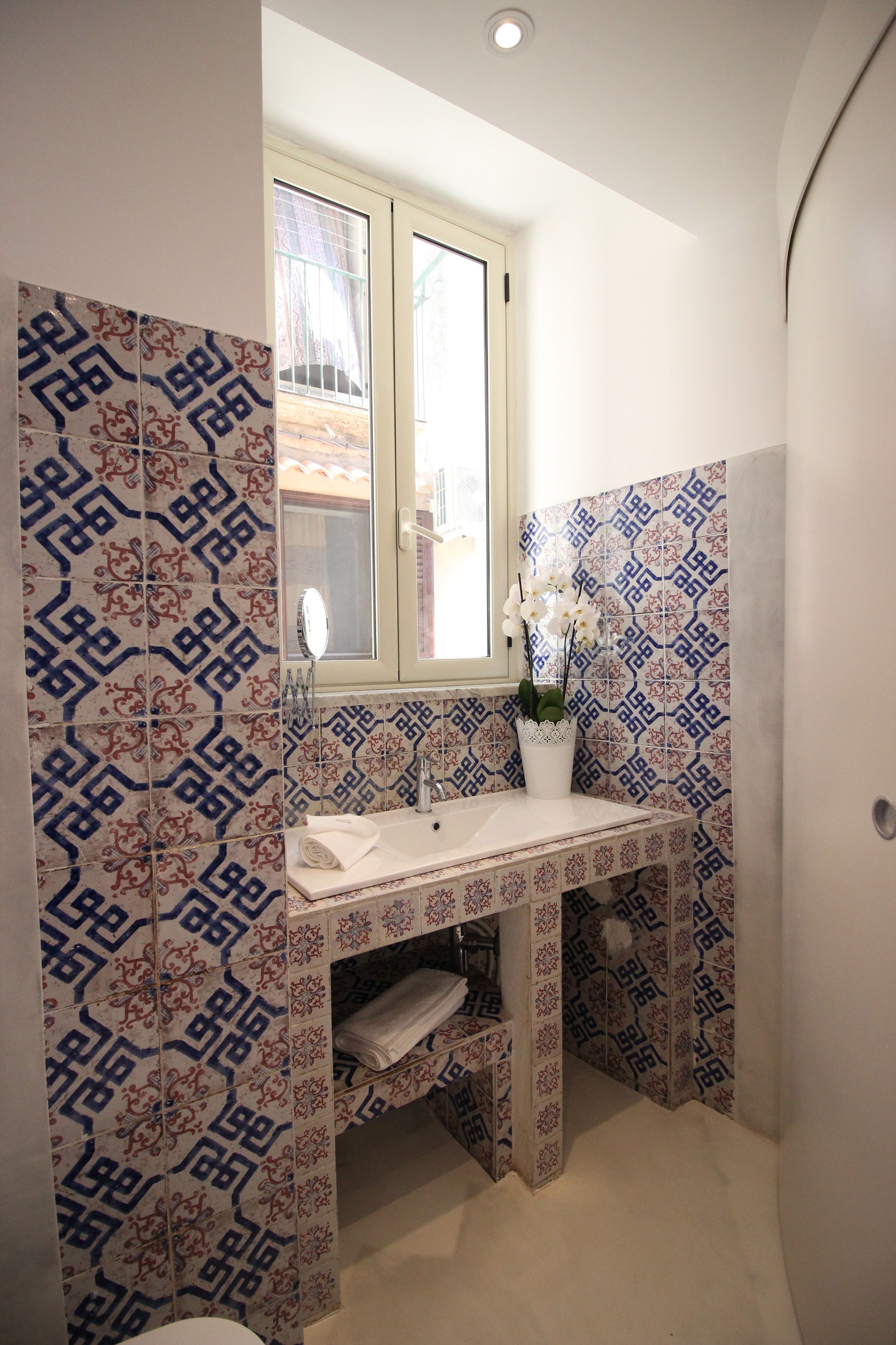 Un bany amb rajoles de disseny, una finestra, un lavabo i un mirall.