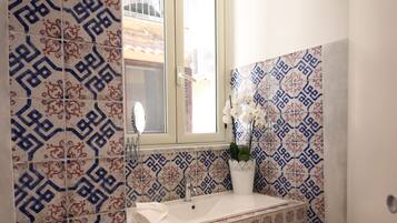 Un bany amb rajoles de disseny, una finestra, un lavabo i un mirall.