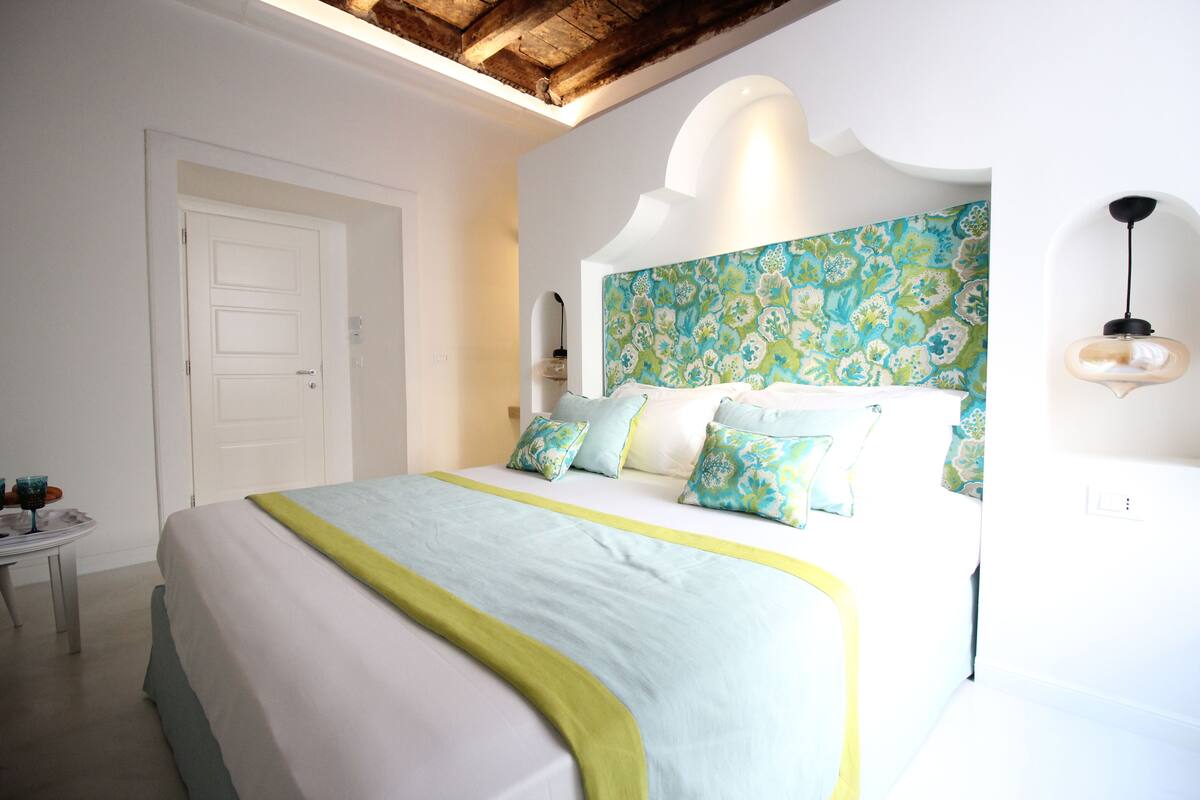 A bedroom with a bed, a bedside table, and a wall with a floral pattern.