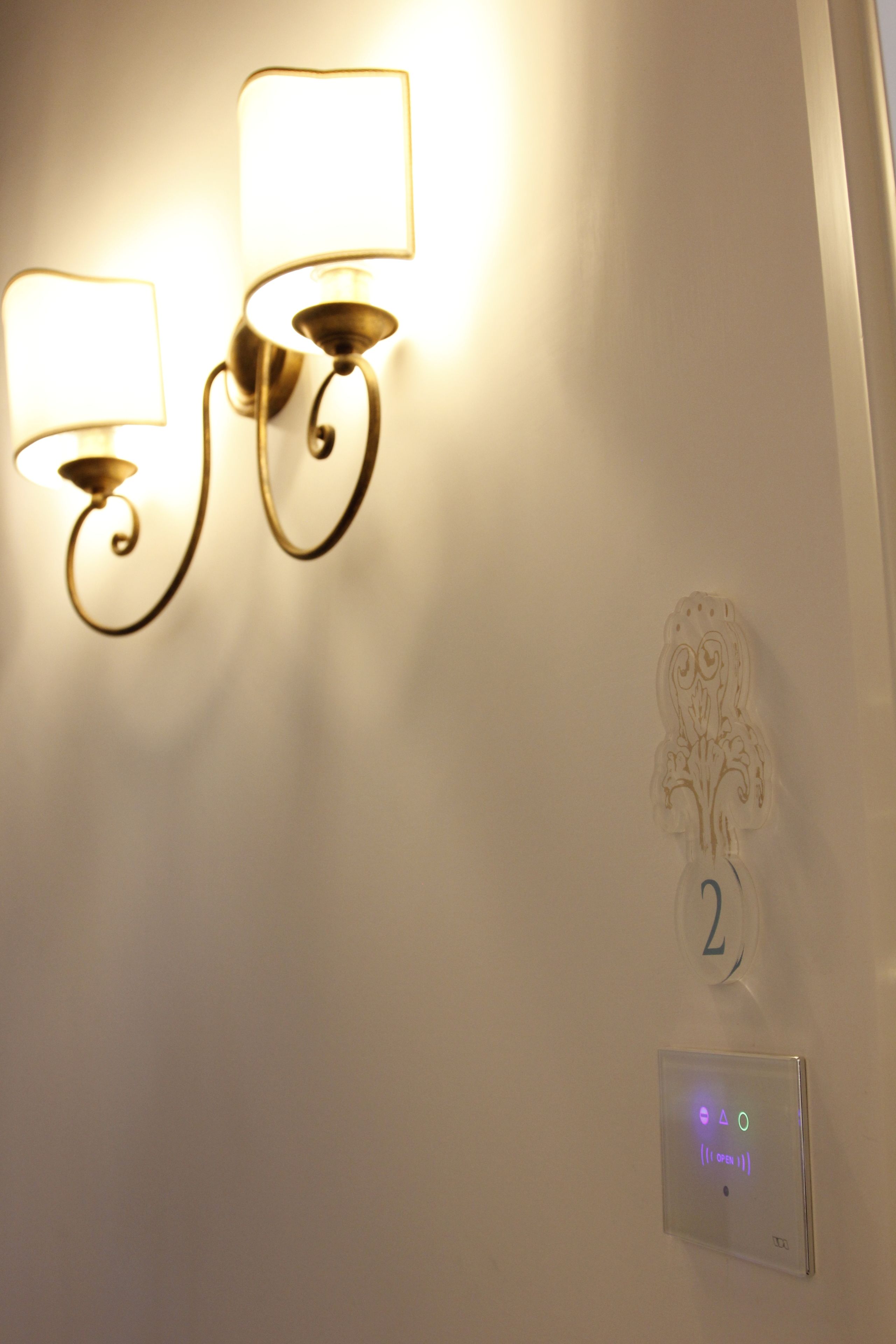Una lámpara de pared con dos luces, una placa decorativa con el número 2 y un panel de control con indicadores iluminados.