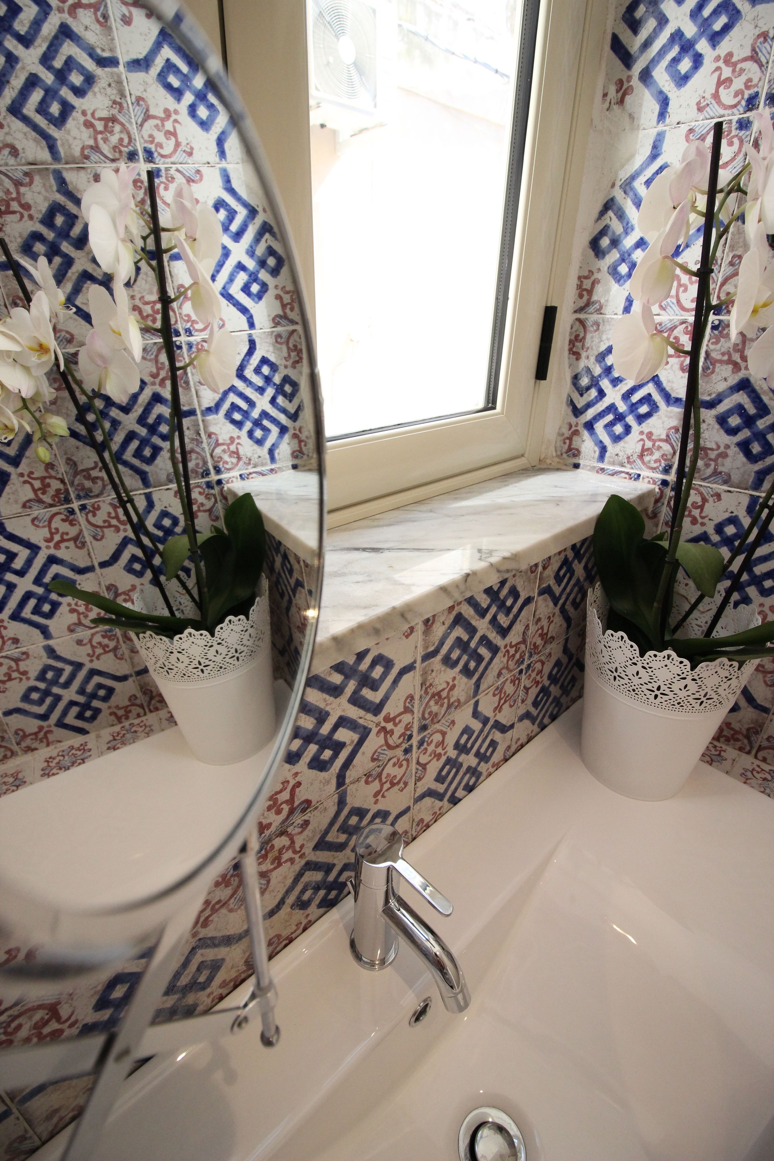 A bathroom with a sink, mirror, and two orchid plants in white vases.