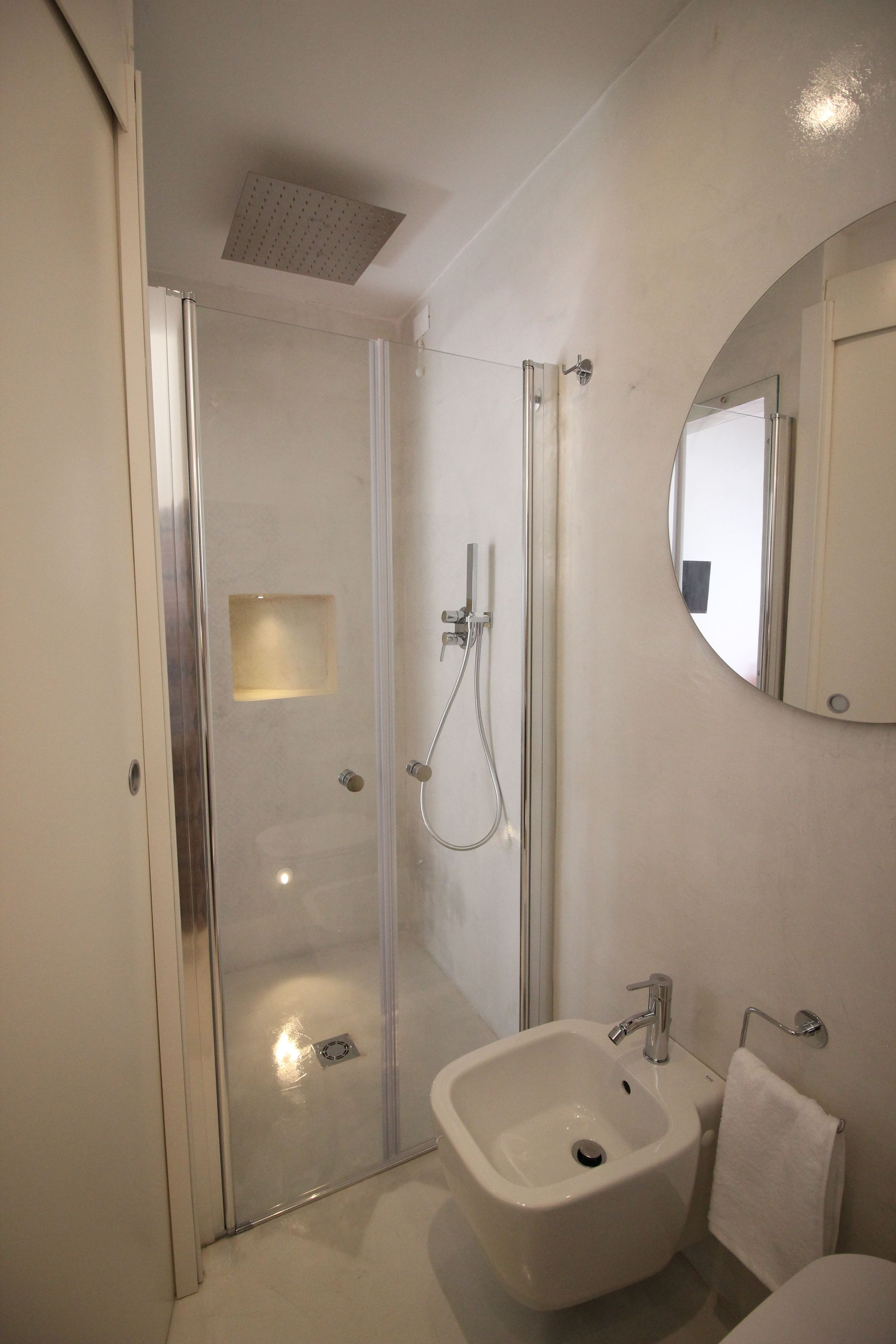 A modern bathroom with a glass-enclosed shower, a white sink, and a round mirror.