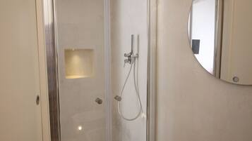 A modern bathroom with a glass-enclosed shower, a white sink, and a round mirror.