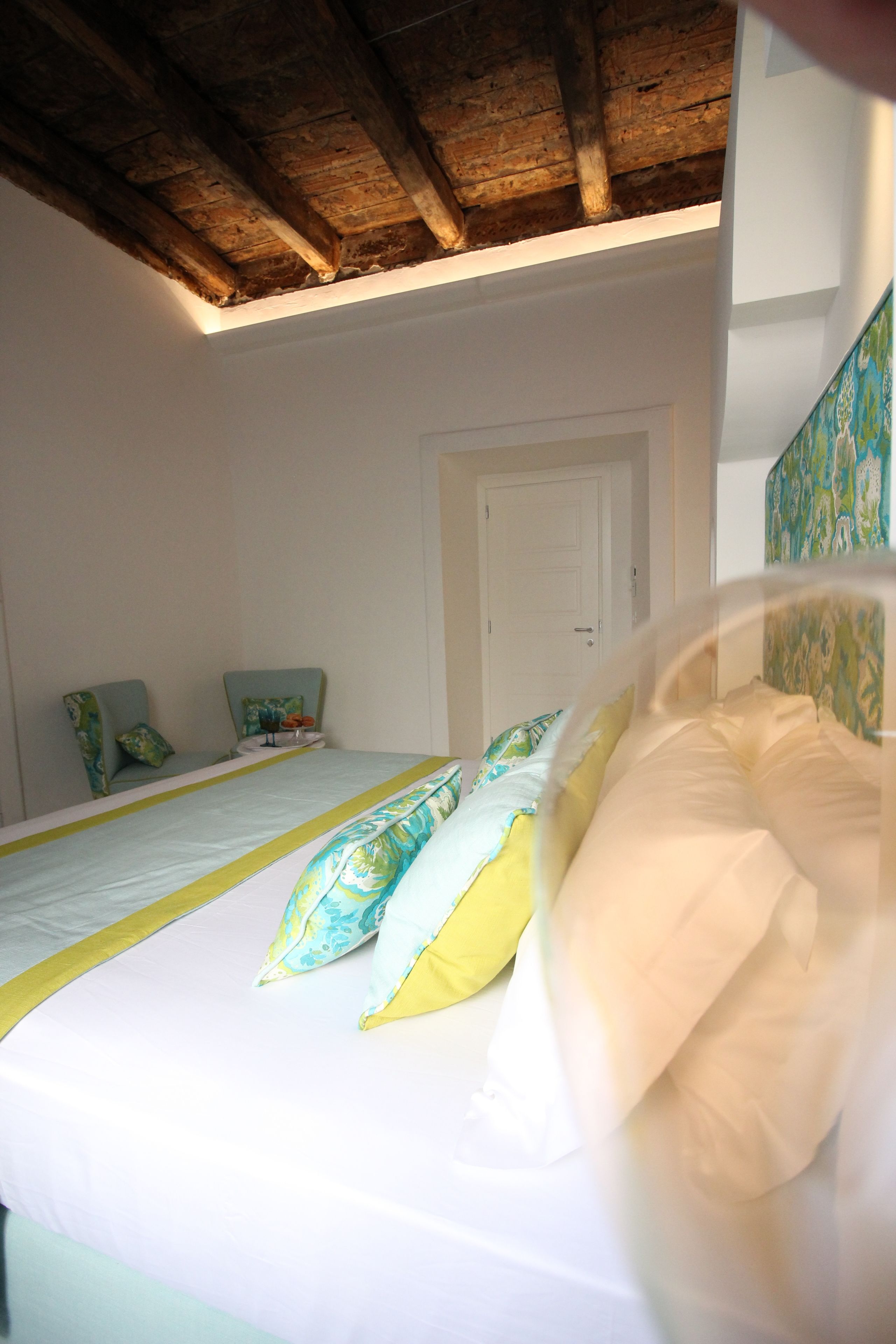 A bedroom with a wooden ceiling, a bed with white and yellow bedding, and two chairs with cushions.