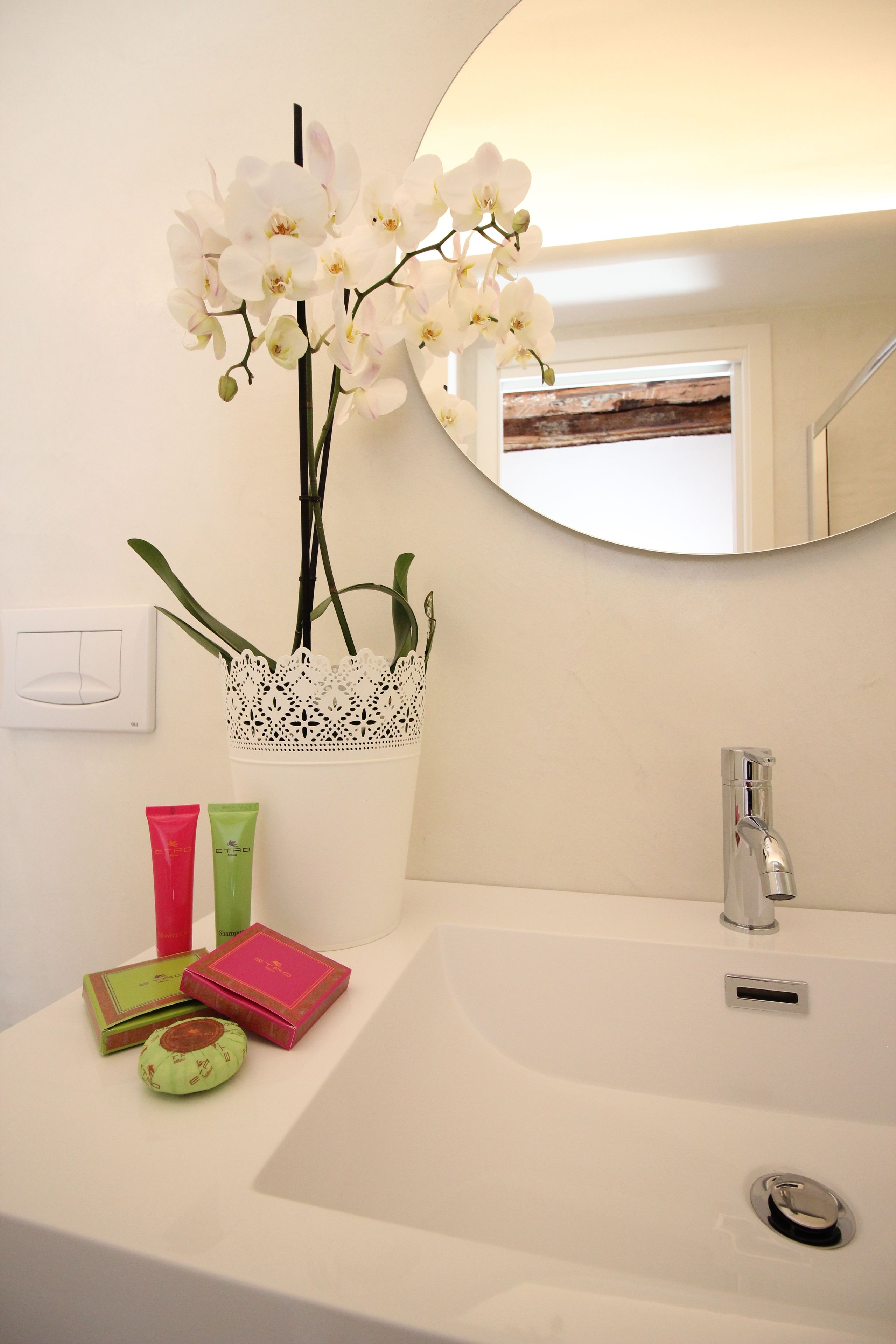 A bathroom with a white sink, a mirror, and a decorative orchid arrangement.