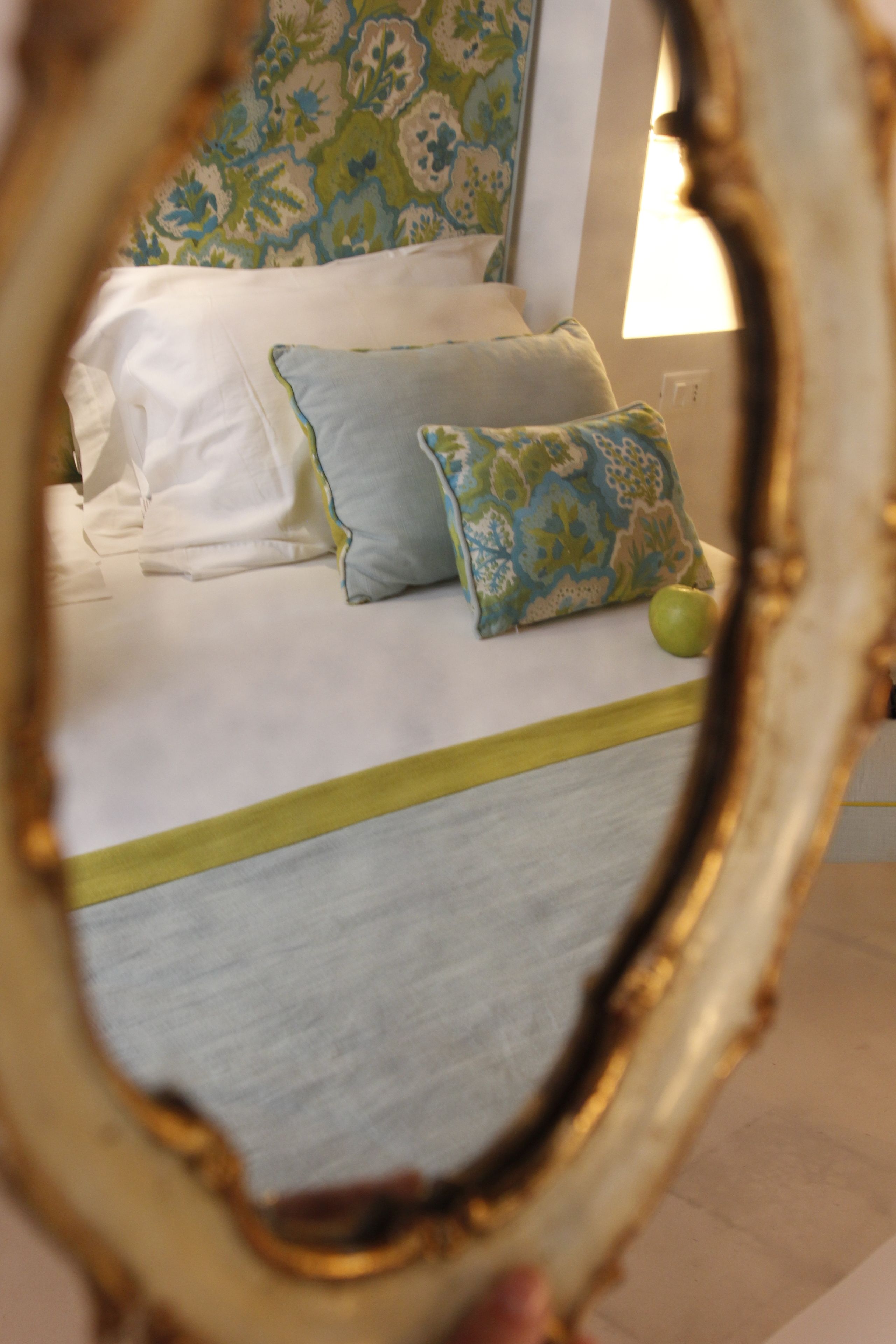 A bed with white linens, a green pillow, and a patterned pillow.