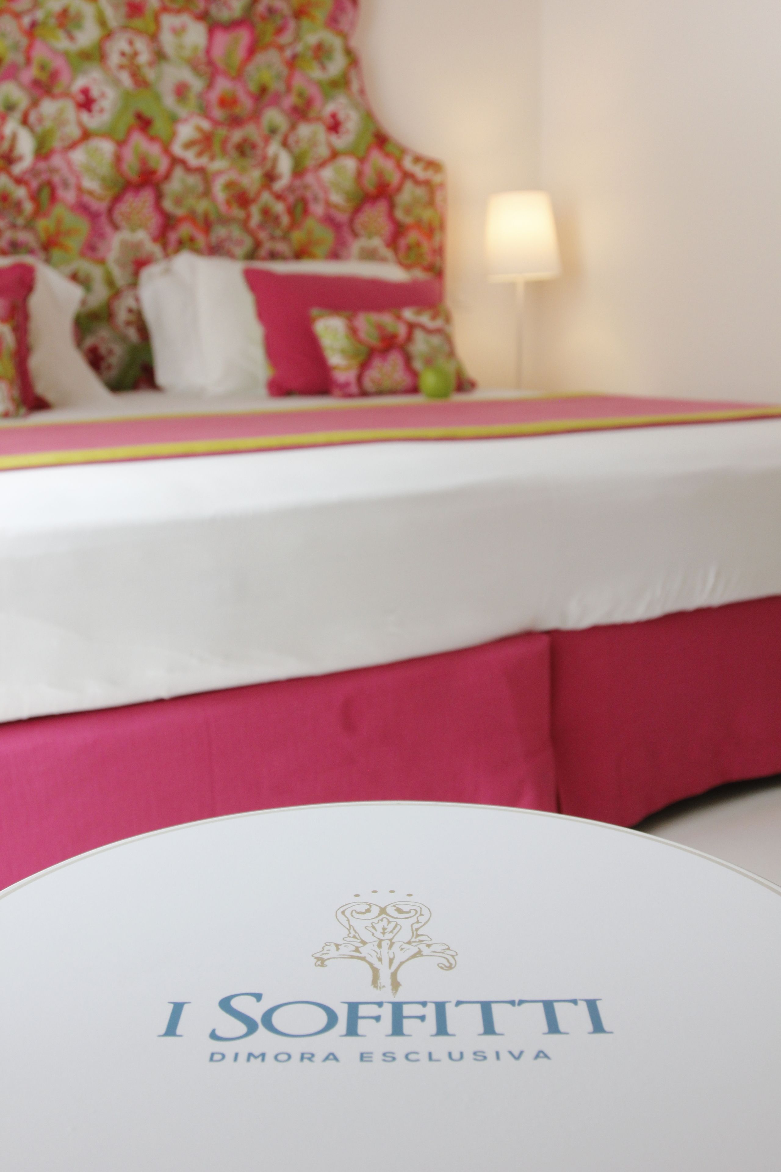 Ein Bett mit weißer und pinkfarbener Bettdecke, einem Blumen-Kopfschild und einer Nachttischlampe.