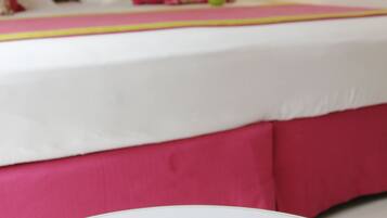 Ein Bett mit weißer und pinkfarbener Bettdecke, einem Blumen-Kopfschild und einer Nachttischlampe.