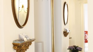 Un baño con un espejo grande, un lavamanos blanco, un estante decorativo con artículos de aseo y una planta en maceta.