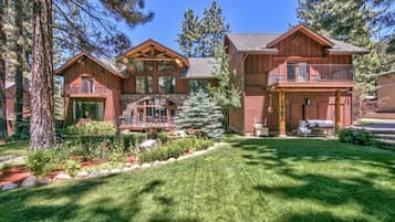 A large wooden cabin with a balcony, surrounded by a well-maintained garden and tall trees.