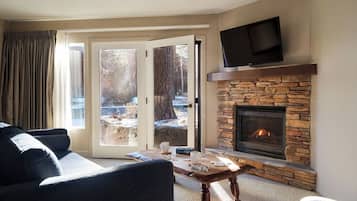 A living room with a stone fireplace, a flat-screen TV mounted above it, and a large window with curtains.