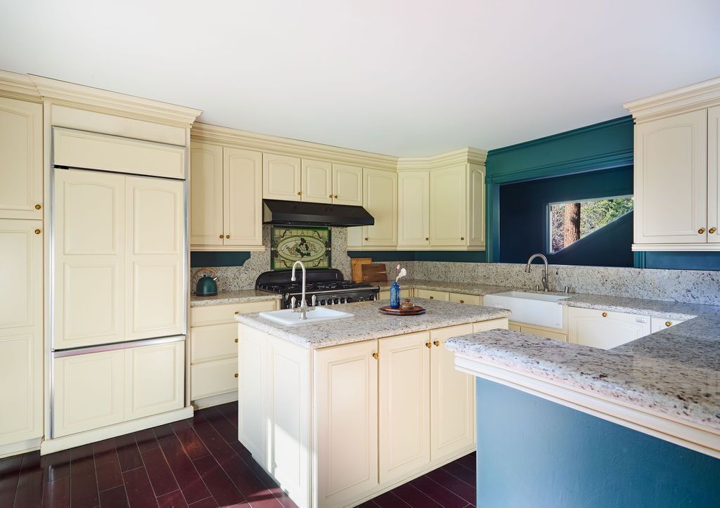 Una cocina con gabinetes color crema, encimera de granito, estufa y pileta.