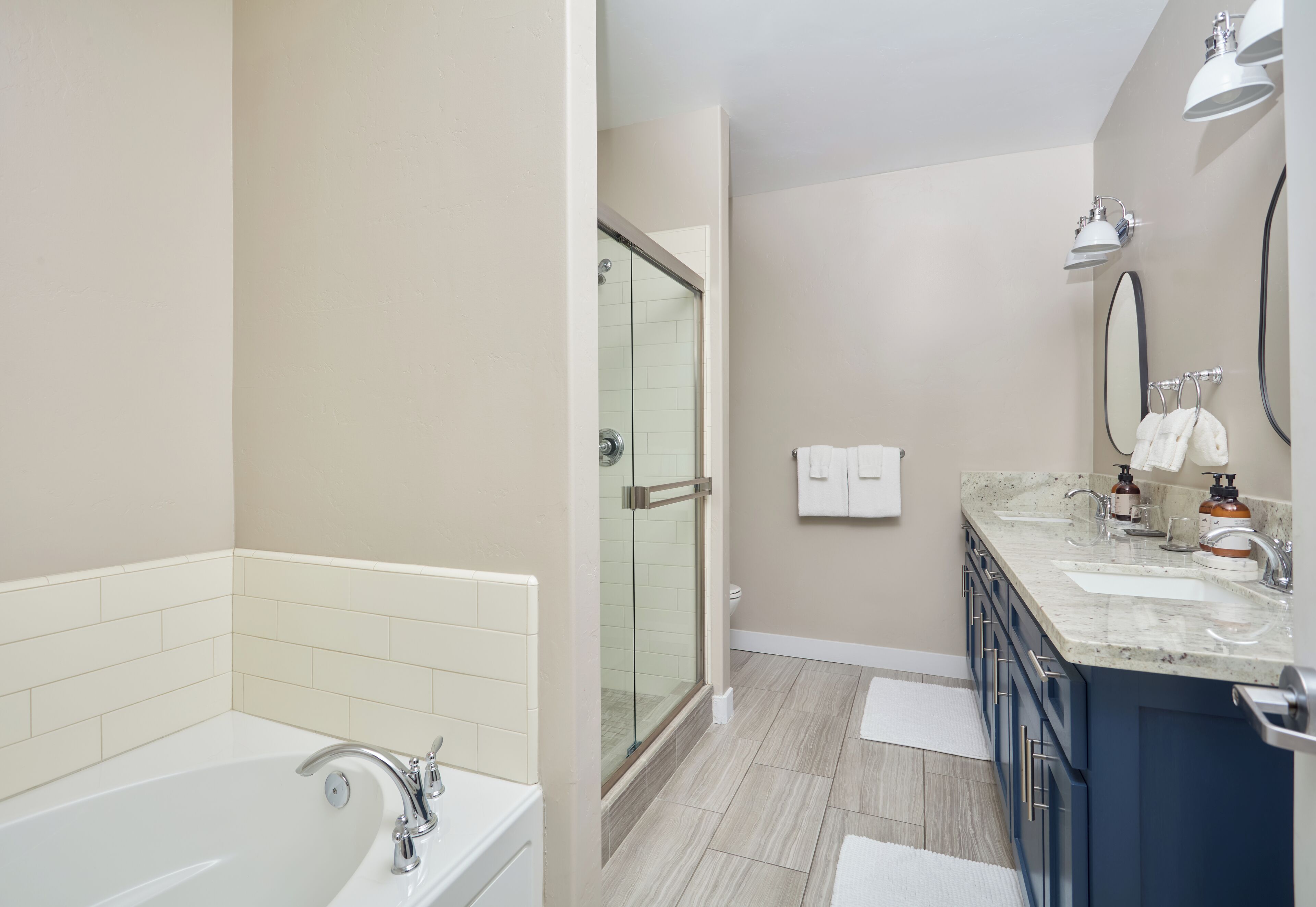 A modern bathroom with a glass-enclosed shower, a bathtub, and a vanity with a sink and mirror.