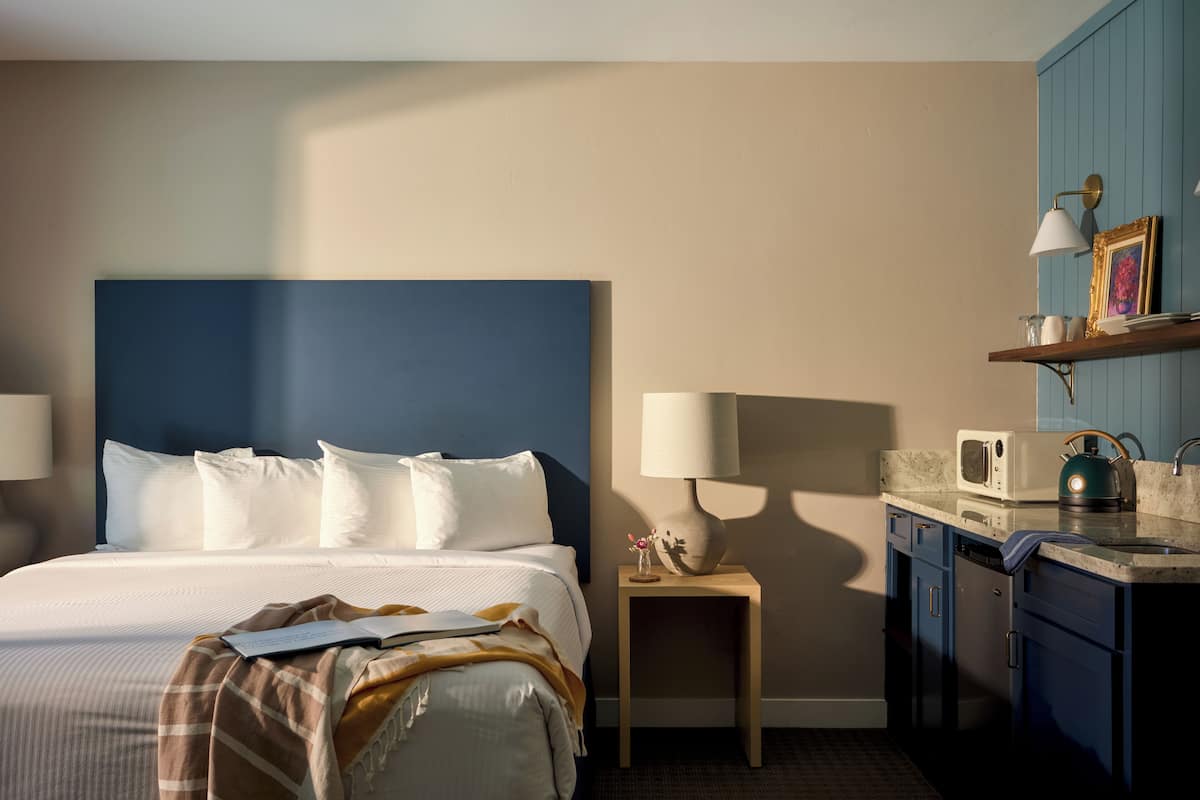 Een hotelkamer met een bed, nachtlampjes, een klein tafeltje met een lamp, een magnetron en een wastafel.