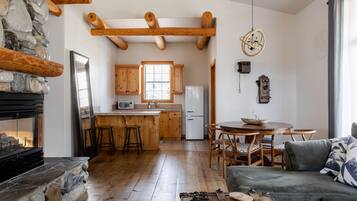 Um interior rústico com lareira de pedra, vigas de madeira, cozinha com armários de madeira, área de refeições com mesa redonda e um espaço de estar aconchegante.