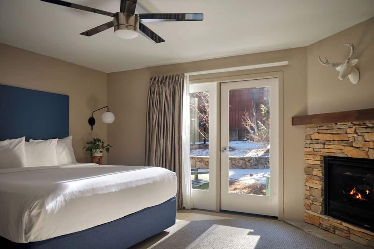 Een slaapkamer met een bed, een plafondventilator, een stenen openhaard en uitzicht op de omgeving.