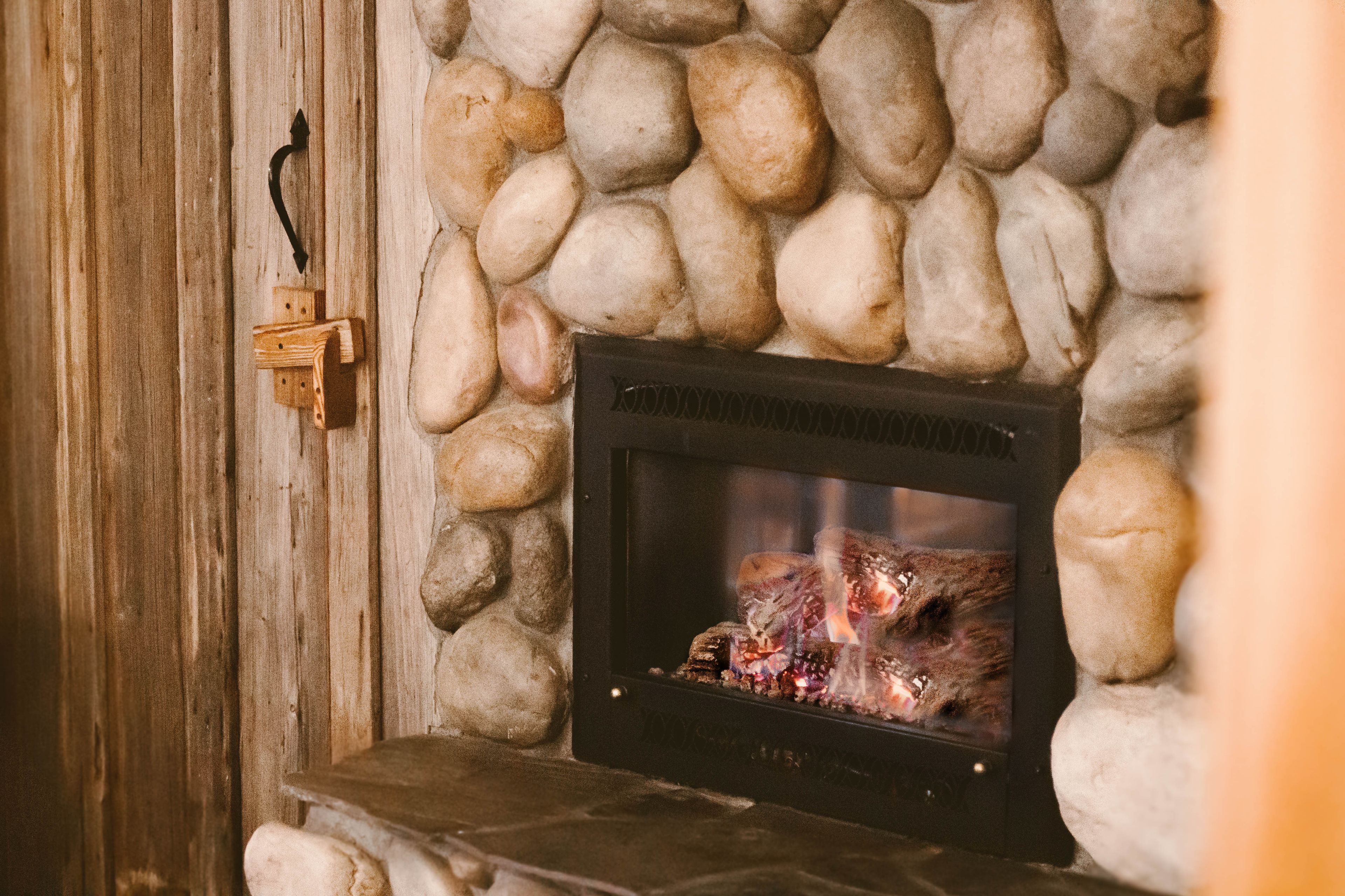 A stone fireplace with a fire burning inside, set against a wooden wall.