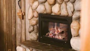 A stone fireplace with a fire burning inside, set against a wooden wall.