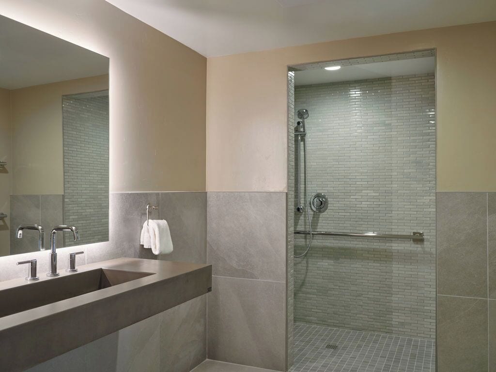 Une salle de bain moderne avec un grand miroir, un lavabo à deux robinets et une douche séparée par une paroi de verre.