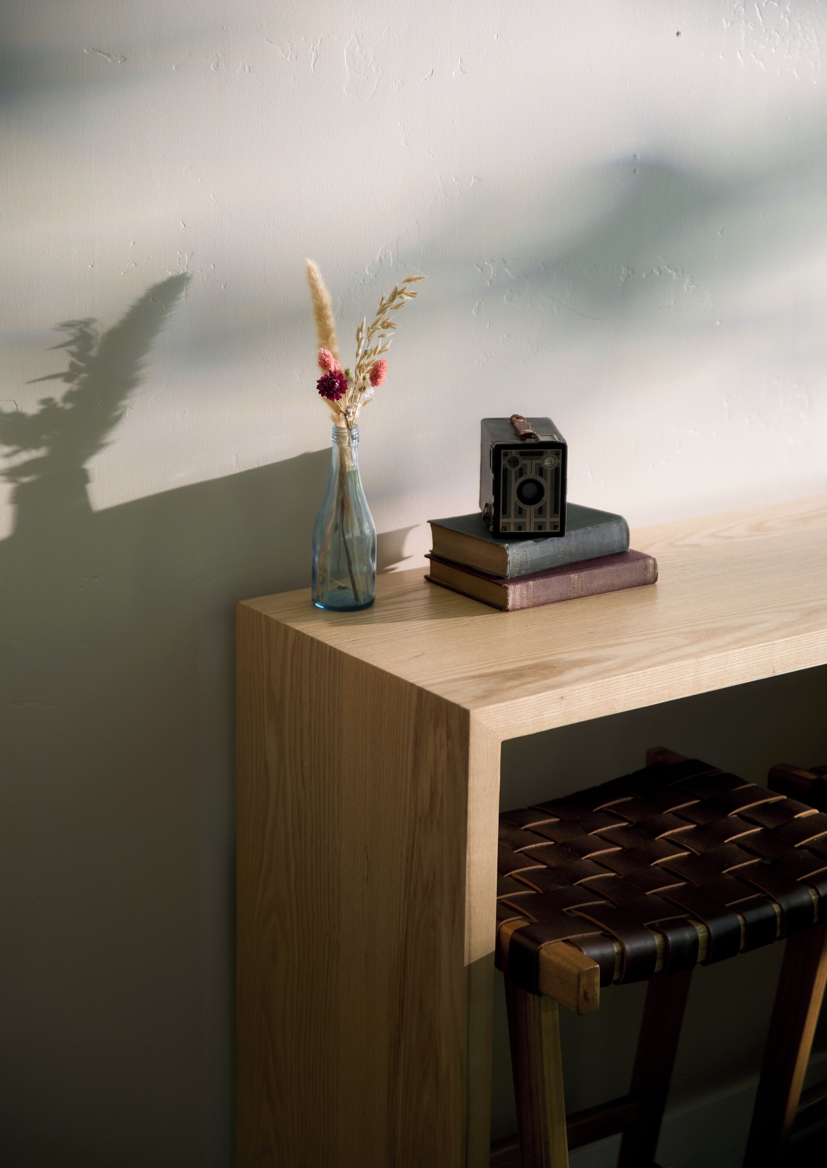 A wooden desk with a vase of dried flowers, a camera, and books.