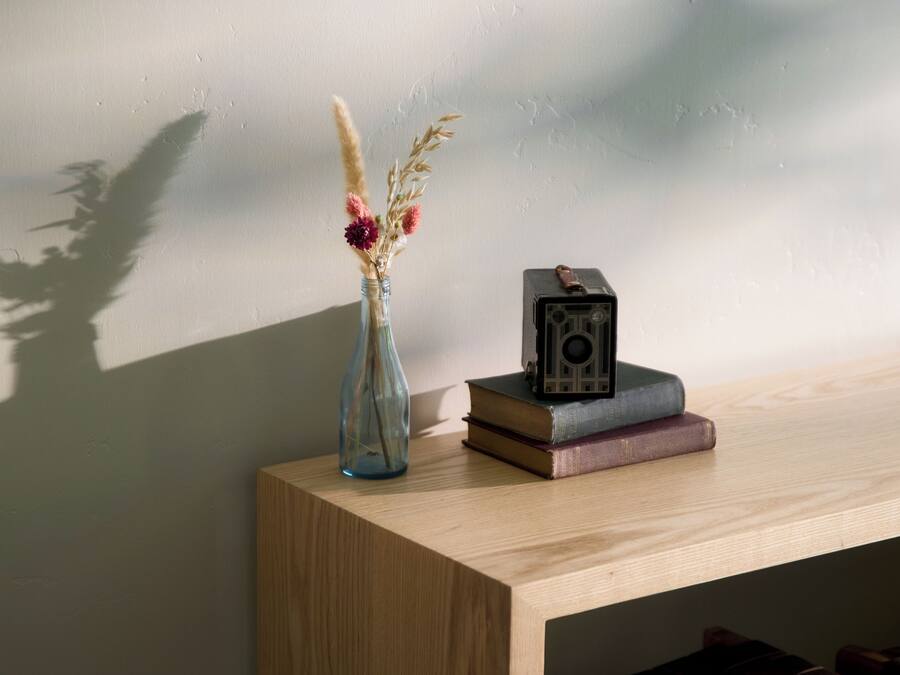 A wooden desk with a vase of dried flowers, a camera, and books.