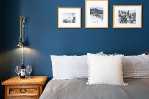 Un dormitorio con cama, almohadas, una mesita de noche con una botella y vasos, y tres cuadros enmarcados en la pared.